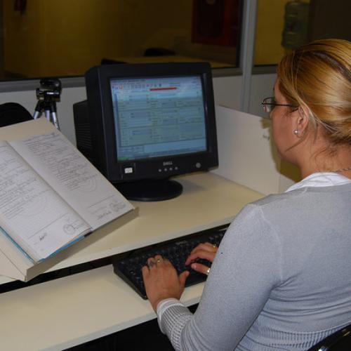 Woman working at her computer with an open book beside her. Photo credit: Mia Harbitz